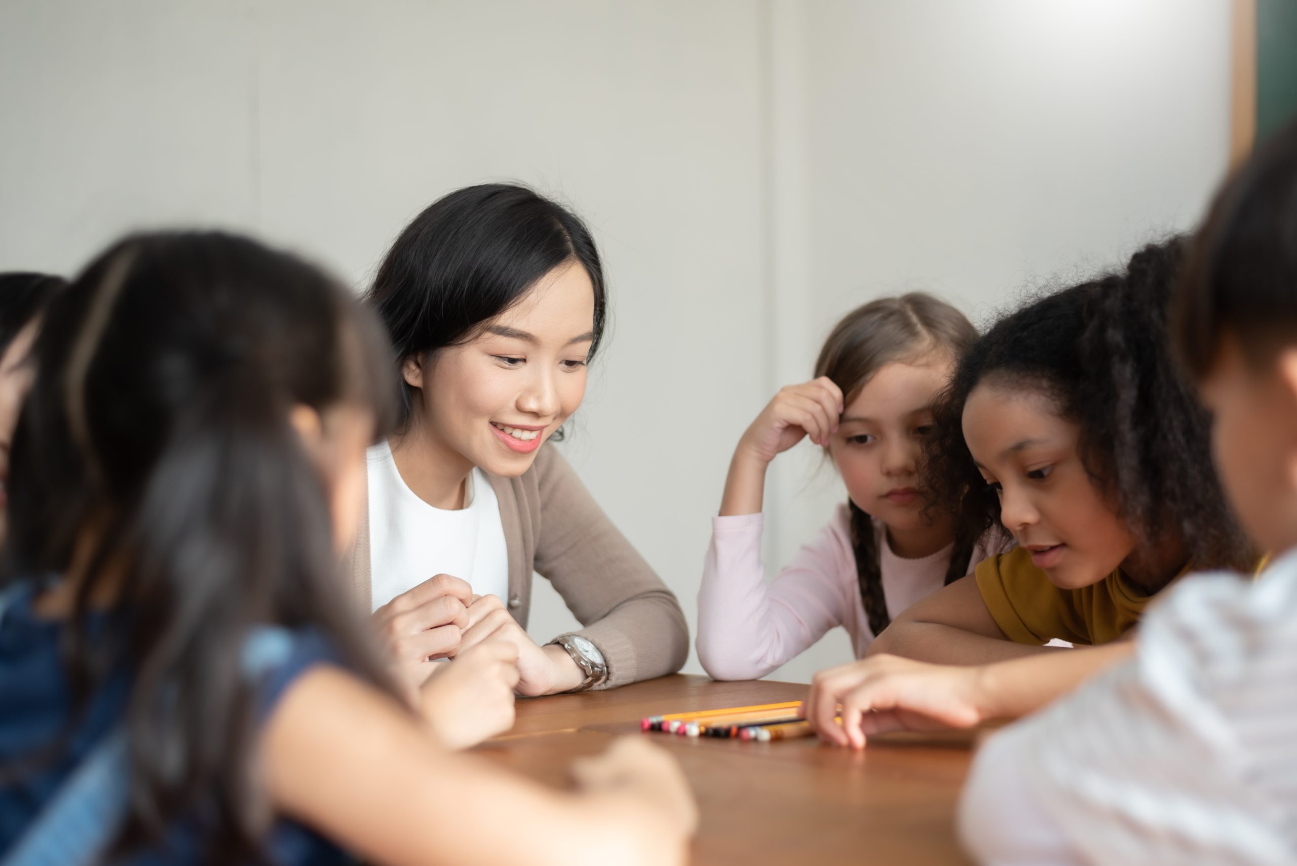 Pupils,Playing,Games,With,Asian,Female,Teacher,Together,In,Classroom.